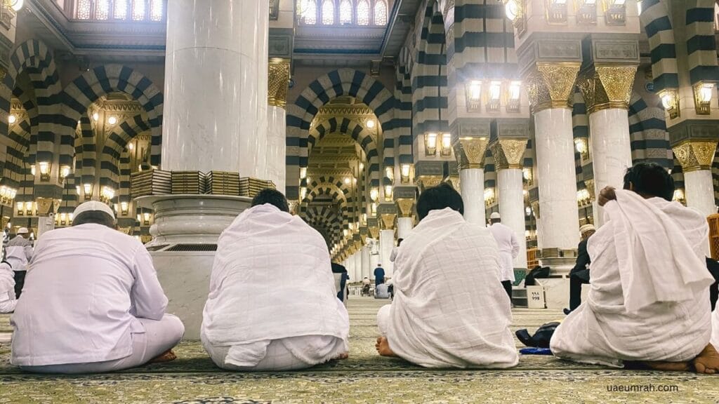 Muslim pilgrims in white Ihram clothing sitting inside Al-Masjid an-Nabawi, Medina, during Umrah.
